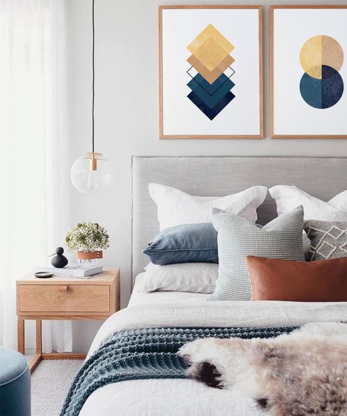 Sweet Dreams: Our 2020 Bedroom Interior Trend Predictions by Fashion Du Jour LDN. Close-up of abstract geometric wall art and a grey velvet upholstered bed frame, pillows in a variety of textures including knitted, wooden bedside table in a grey, white, navy, mustard and terracotta bedroom interior