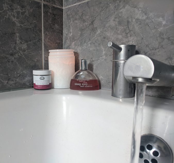 Bathroom with white bath and grey marble tiles, white candle and bath products