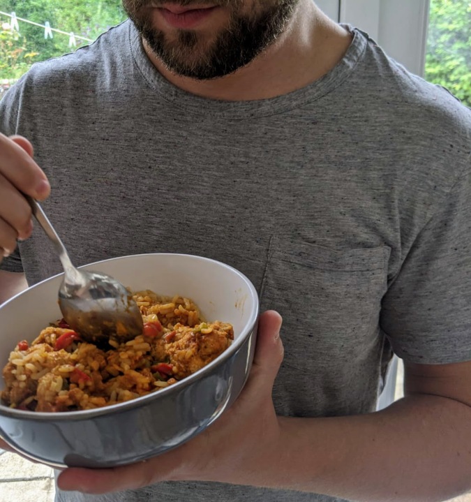 Small Prices Big Gains How Musclefood Can Transform Your Meal Time And You By Fashion Du Jour LDN. Bearded muscly man in a grey t-shirt eating Musclefood Prepped Pots Moroccan Pork Meatballs and Cous Cous 