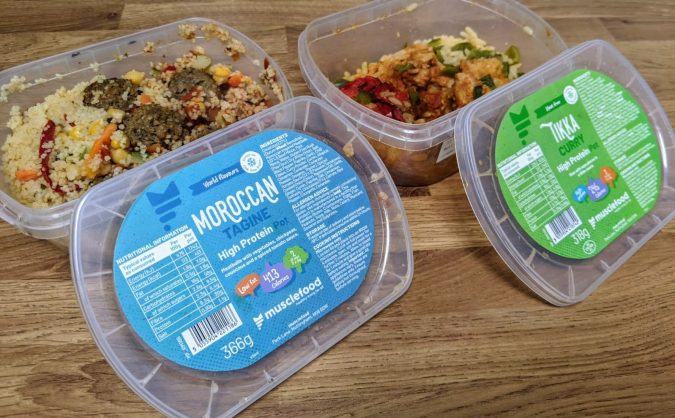 Small Prices Big Gains How Musclefood Can Transform Your Meal Time And You By Fashion Du Jour LDN. Muscle Food Prep Pots Moroccan Pork Meatballs and Cous Cous and Meatfree Mock Chicken Tikka on wooden kitchen worktop